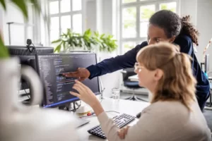 Two women's pointing the monitor.