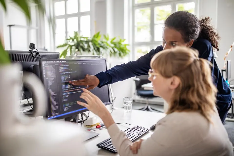 Two women's pointing the monitor.